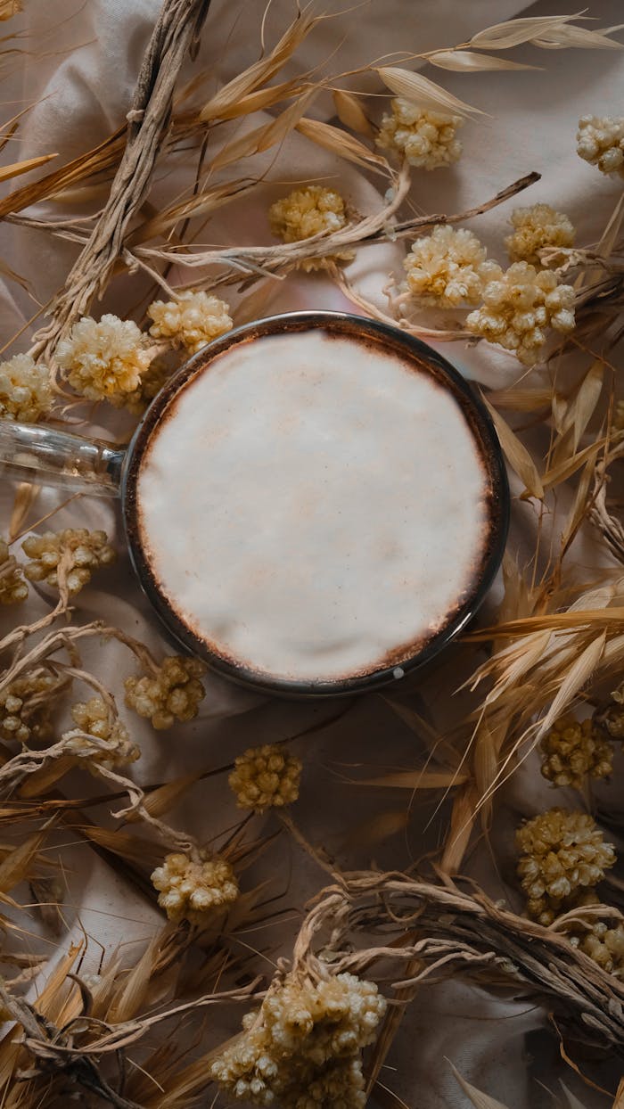 A cozy rustic coffee setting with dried grains and flowers around a frothy cup.