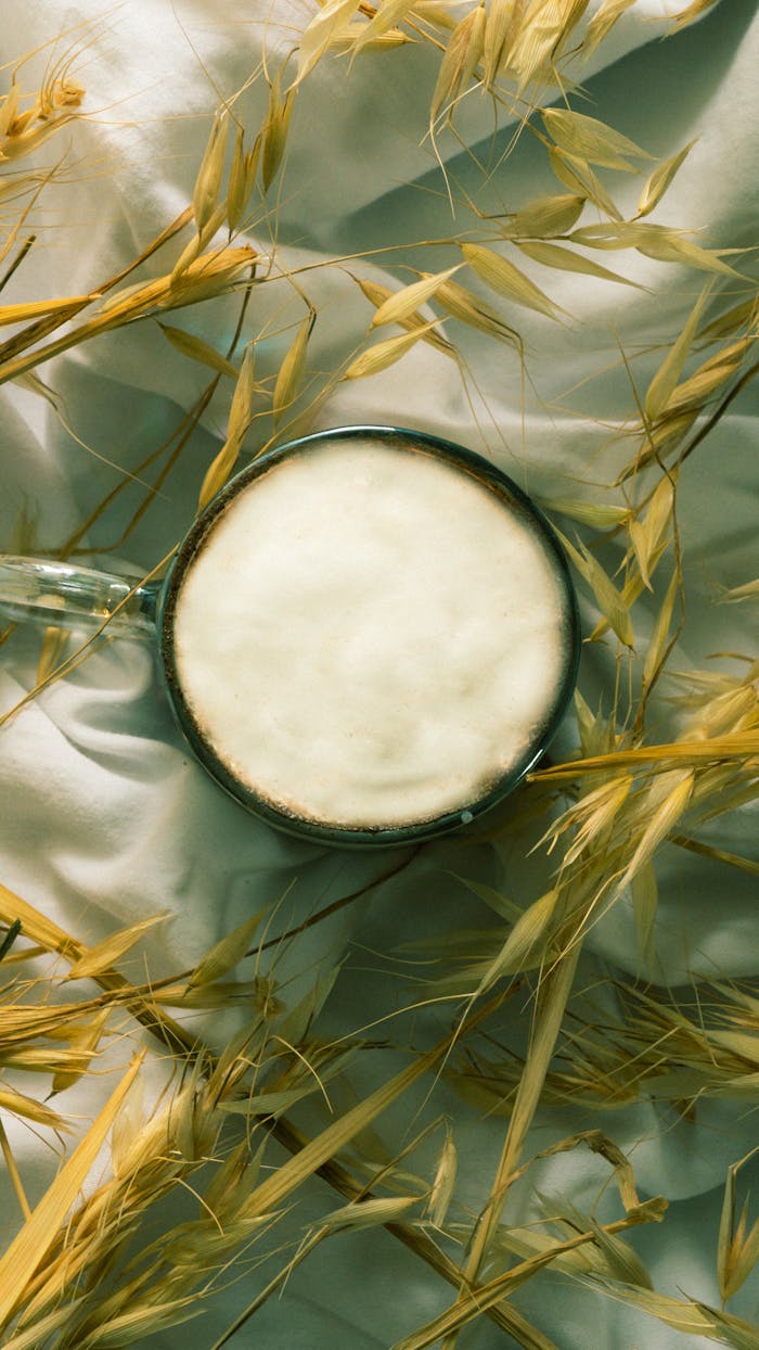 Top view of a foamy drink in a rustic setting surrounded by grain on a white sheet.