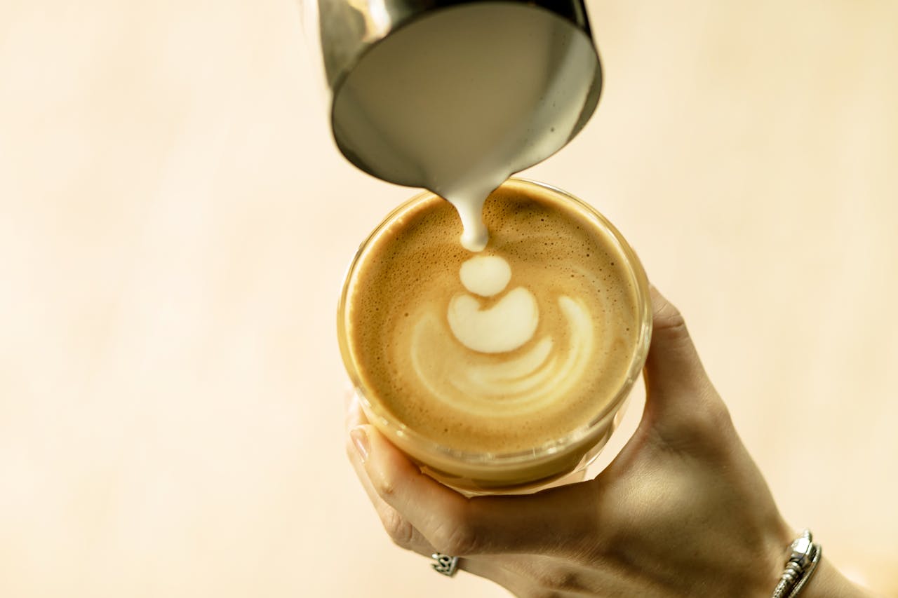 A hand pouring milk to create latte art in a coffee cup, top view.
